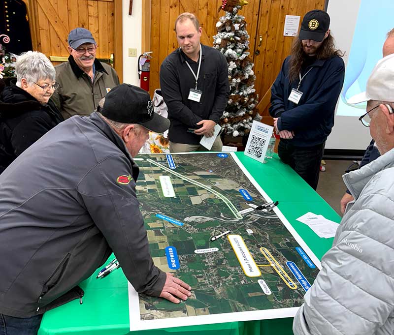 Open house attendees gather around a large map (roll plot) of the project area. 